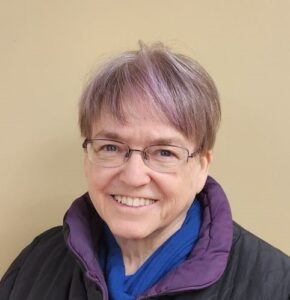 Susi McCune smiling, with purple-tinted hair and a purple jacket